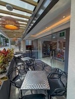 Un café al aire libre con mesas y sillas, un acceso por puerta de cristal y vistas a una tienda.