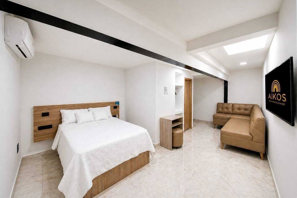 A modern hotel room with a bed, a sofa, a TV, and a ceiling fan.