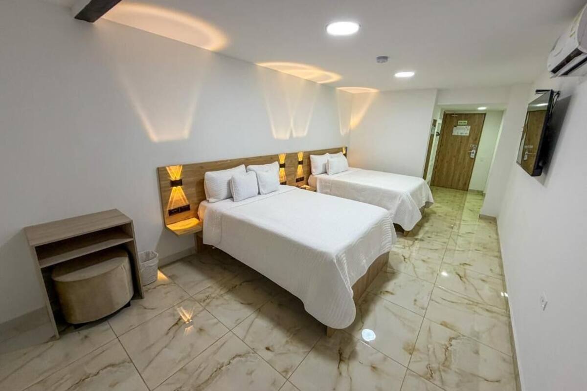 A hotel room with two beds, a wooden headboard, a small seating area, and a tiled floor.