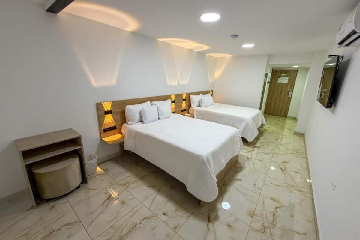 A hotel room with two beds, a wooden headboard, a small seating area, and a tiled floor.