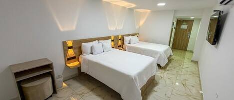 A hotel room with two beds, a wooden headboard, a small seating area, and a tiled floor.
