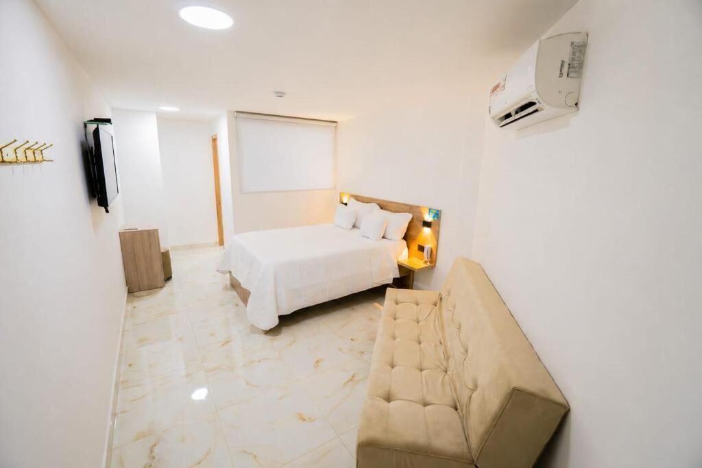 A hotel room with a bed, a sofa, a wall-mounted air conditioner, and a door leading to another room.