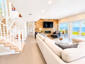 Ein modernes Wohnzimmer mit Kamin aus Stein, einem Flachbildfernseher, einem großen Sofa und einer Treppe mit weißen Geländern.