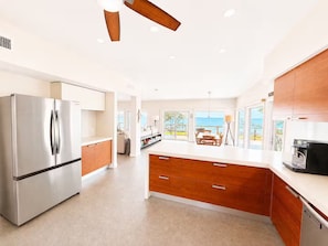 Eine moderne Küche mit einem Edelstahl-Kühlschrank, Holzschränken, einer großen Kochinsel und Meerblick.