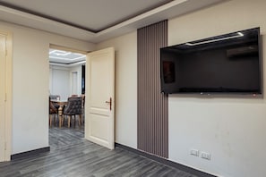 Un passadís amb una zona de menjador, un televisor de pantalla plana fixat a la paret i una porta que dona a una altra habitació.