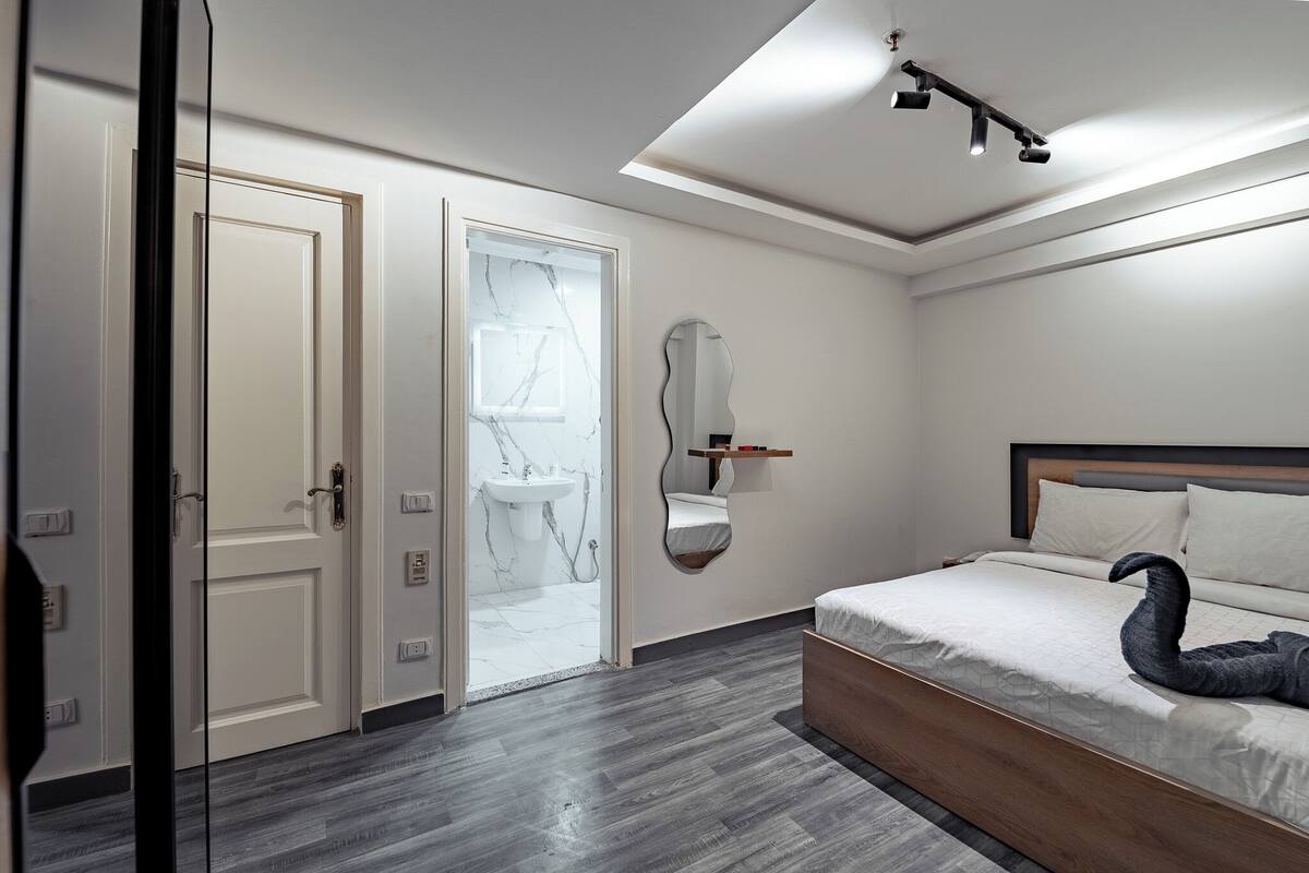 A modern bedroom with a bed, a mirror, and a bathroom with a marble sink.