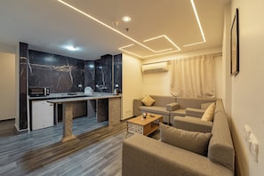 Ein modernes Wohnzimmer mit Sofa, Couchtisch und Küchenzeile mit Mikrowelle und kleinem Kühlschrank.