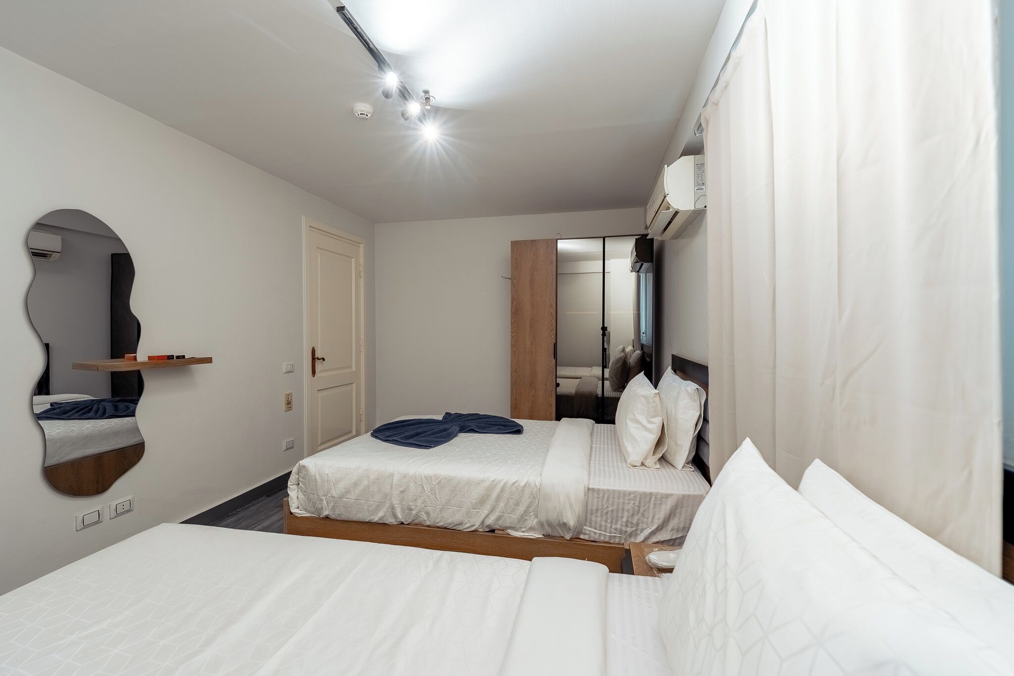 Una habitación de hotel con cama, espejo, puerta y una lámpara en el techo.