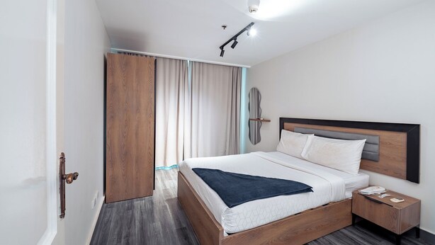 Una habitación de hotel moderna con una cama de madera, una mesita de noche, un armario y una lámpara de techo.