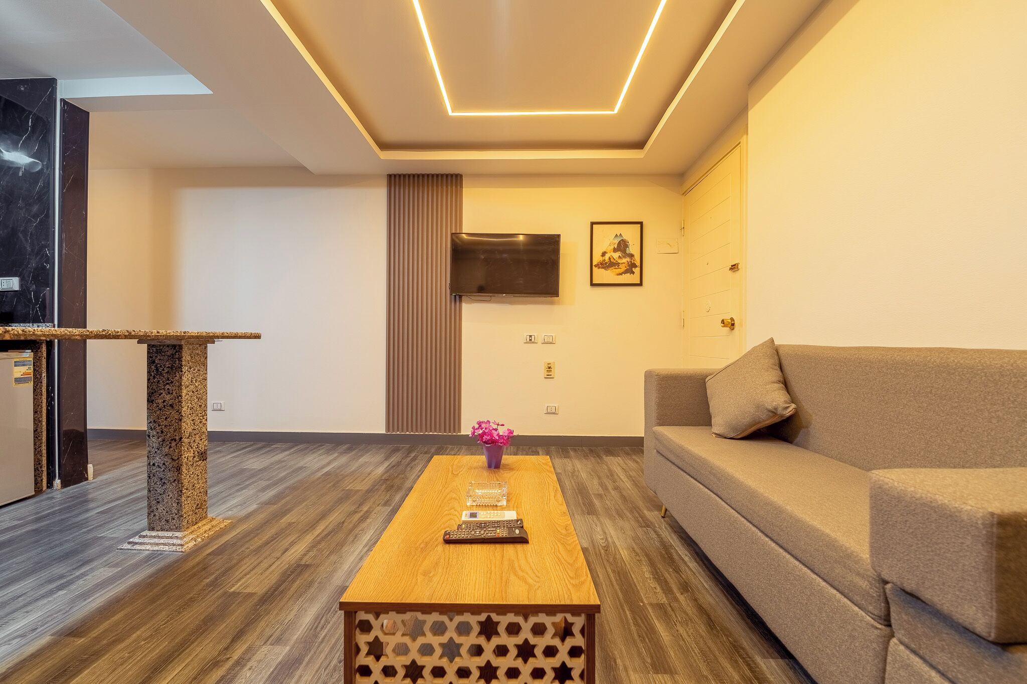 Una sala moderna con una mesa de centro de madera, un sofá, un televisor montado en la pared y un jarrón decorativo.