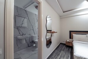Ein modernes Badezimmer mit Marmorwand, Waschbecken und Toilette. Ein Bett mit Holz-Kopfteil und ein Nachttisch sind ebenfalls vorhanden.