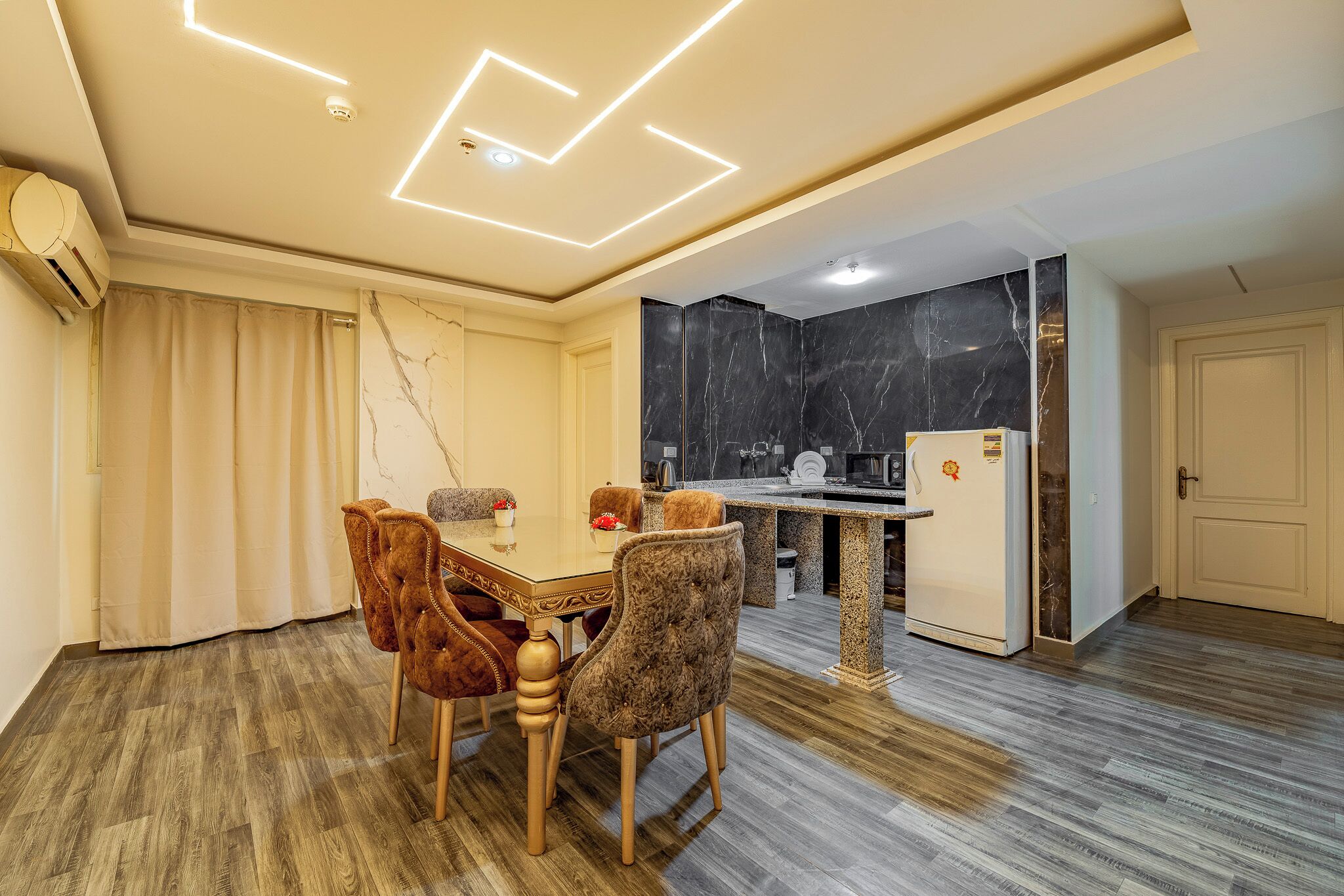 Cozinha moderna com revestimento de mármore, área de refeições com mesa e cadeiras, e geladeira separada.