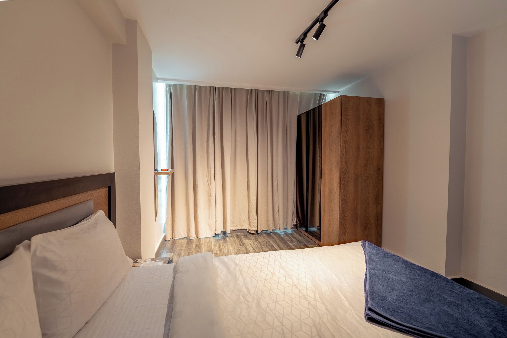 A hotel room with a bed, a wooden wardrobe, and a window with curtains.