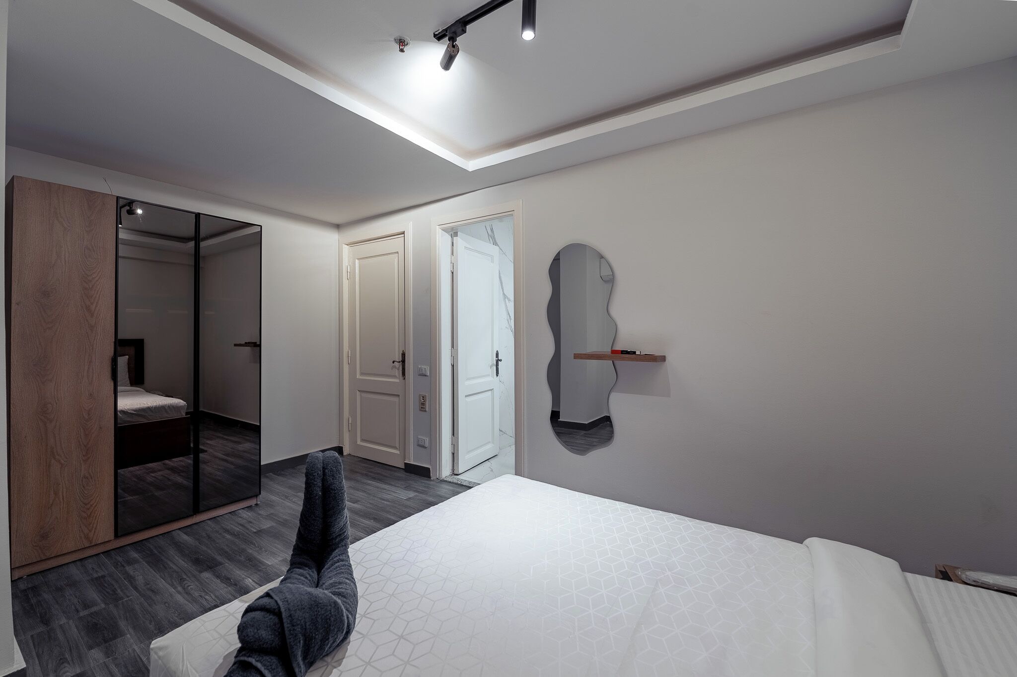 A modern bedroom with a bed, a wardrobe, a mirror, and a door.