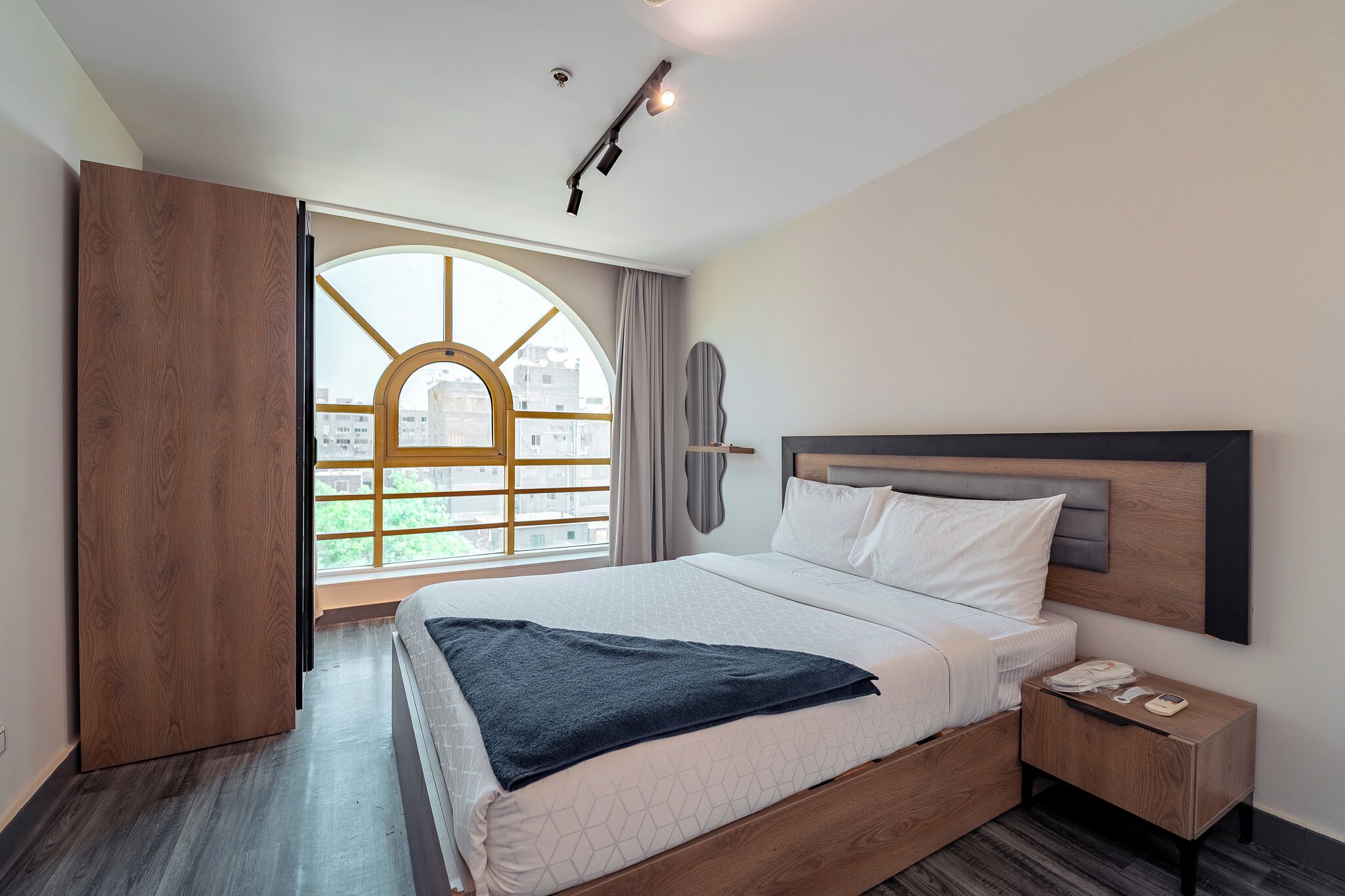 Camera da letto moderna con un letto grande, un armadio in legno, un comodino con un telefono e vista sugli edifici attraverso una finestra.