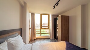 Habitación de hotel con cama, armario, ventana con cortinas y vistas a la ciudad.