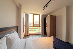 Una habitació d'hotel amb un llit, un armari, una finestra amb cortines i vista a la ciutat.