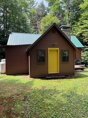 A small wooden cabin with a green roof, a yellow door, and a chimney. - Quaint 2-bedroom cabin on Oxbow Lake perfect for relaxing Adirondack getaways (Lake Pleasant)