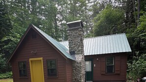 Una cabaña con chimenea de piedra, puerta amarilla y techo de metal.
