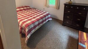 Un dormitorio con cama, cómoda, ventana con cortinas y un cuadro en la pared.
