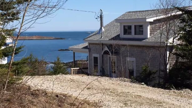 A house with a stone exterior, a small porch, and a view of the ocean. - Charming 3-bedroom cottage in lovely Vinalhaven perfect for relaxing (Vinalhaven)