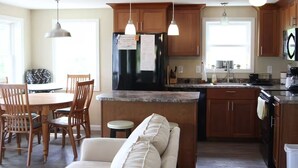 A kitchen with wooden cabinets, a black refrigerator, a dining area with a table and chairs, and pendant lighting. - Charming 3-bedroom cottage in lovely Vinalhaven perfect for relaxing (Vinalhaven)