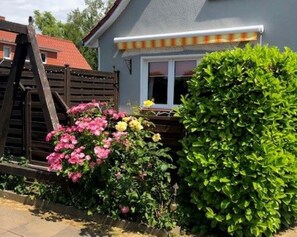 Ein Haus mit Holzzaun, Fensterläden in Weiß und verschiedenen blühenden Pflanzen.