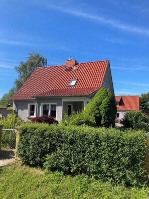 Ein zweistöckiges Haus mit rotem Ziegeldach, einem kleinen Fenster und einer gepflegten Hecke davor.