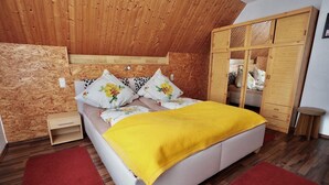 Une chambre avec un plafond en bois, un lit agrémenté d’oreillers à motifs floraux, une couverture jaune, une armoire en bois et un tapis rouge.