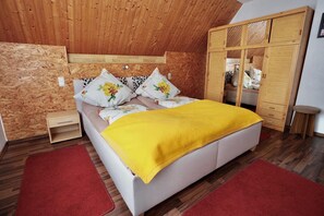 Ein Schlafzimmer mit Holzbalkendecke, einem Bett mit blumigen Kissen, einer gelben Decke, einem Holzschrank und einem roten Teppich.