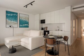 A modern kitchen with white cabinetry, a dining area with a round table and chairs, and two large abstract paintings on the wall. - Stylish 2BR Retreat in Prime São Bento (Lisbon)