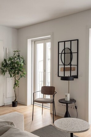Ein Zimmer mit Holzboden, einer Topfpflanze, einem Sessel, einem runden Tisch und einer Wandleuchte.