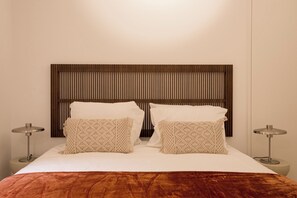 Ein Doppelbett mit Holz-Kopfteil, zwei Nachttische und eine rote Tagesdecke.