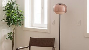 Et værelse med en træstol, en gulvlampe, en potteplante og et vindue.