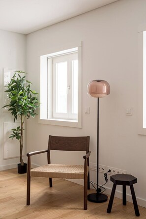 A room with a wooden chair, a floor lamp, a potted plant, and a window. - Charming 2BR with Private Patio in São Bento (Lisbon)