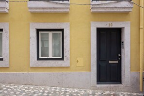 Ein Gebäude mit gelber Fassade, einer schwarzen Tür mit der Nummer 10 und einem Fenster mit weißem Rahmen.