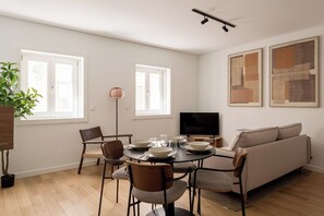 A modern living room with a dining table, chairs, a sofa, a TV, and artwork on the walls. - Charming 2BR with Private Patio in São Bento (Lisbon)