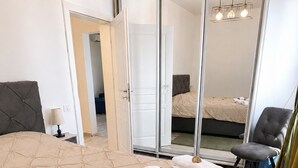 Una habitación de hotel con una cama grande, un espejo, una silla, un escritorio con lámpara y una puerta corredera.
