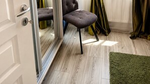Una habitación con puerta corredera de vidrio, una silla tapizada en gris, un tapete verde y vistas de edificios a través de la ventana.