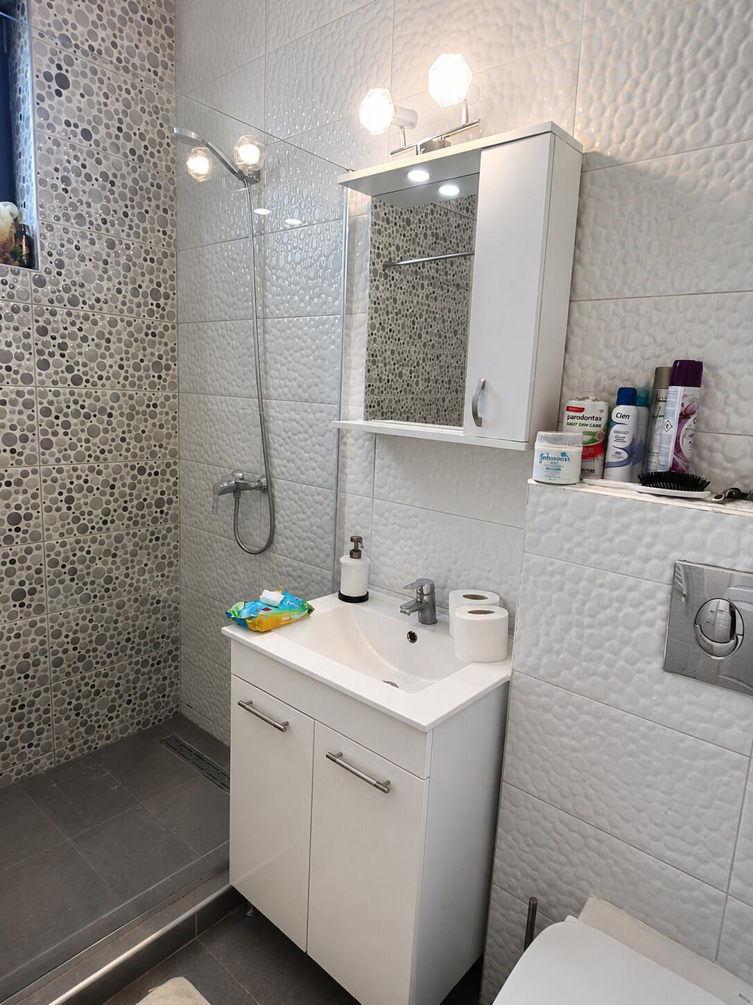 Une salle de bain avec une douche, un lavabo équipé de produits de toilette et un miroir au-dessus du lavabo.