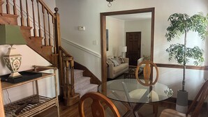A living room with a glass table, wooden chairs, a sofa, a staircase, and a large mirror reflecting the room. - Beautiful Duplex in the heart of Lexington (Lexington)