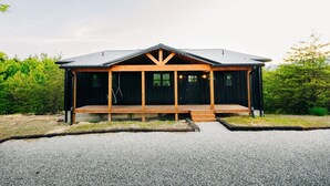 Eine Hütte mit Veranda, einem Schotterweg und bewaldeter Umgebung.