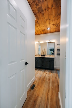 A hallway with wooden flooring, a white door, and a kitchen area with dark cabinets and a countertop. - Red River Gorge Cabin: Hot Tub, Fireplace + Deck (Zachariah)