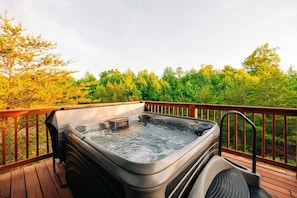 Un jacuzzi en una terraza al aire libre con barandilla de madera y un bosque de fondo.