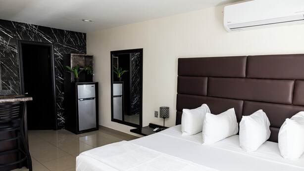 Una habitación de hotel moderna con una cama grande, un refrigerador pequeño, un escritorio con una silla, un espejo y un equipo de aire acondicionado.