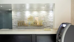 Mostrador de recepción de hotel con pared de piedra de fondo, un cartel de alquiler de coches y un cajero automático.