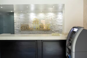 A hotel reception desk with a stone wall backdrop, a car rental sign, and an ATM. - Lovely Studio for Corporates (Charlotte Amalie West)