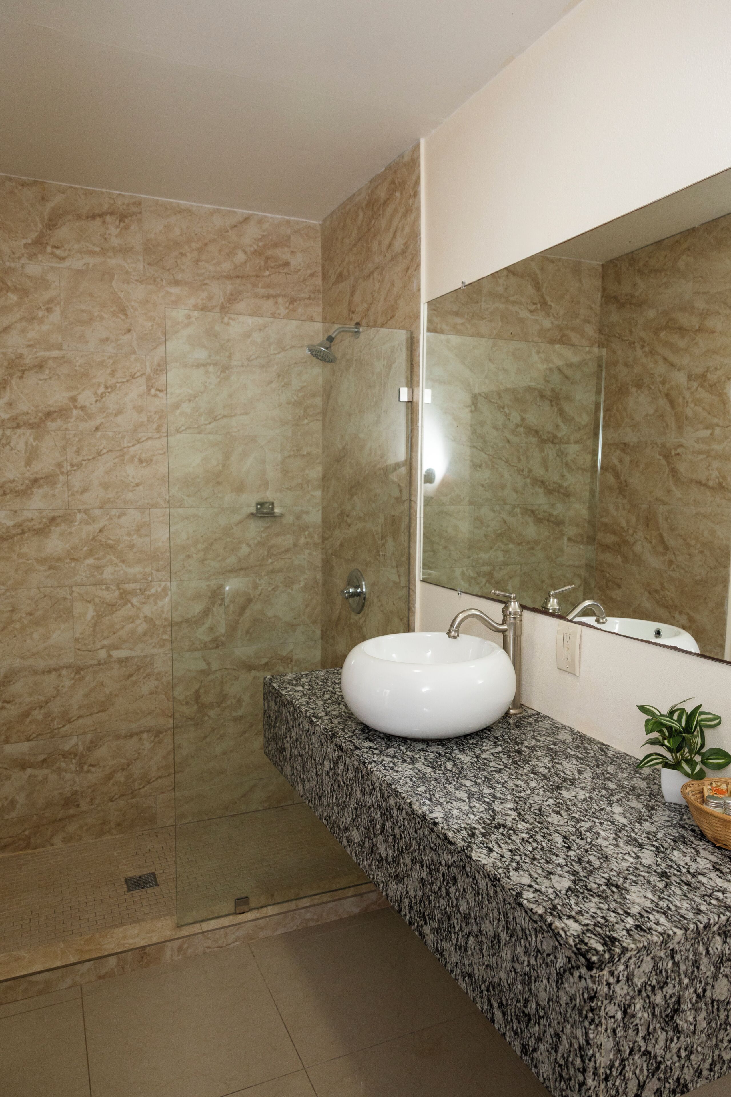 A bathroom with a glass-enclosed shower, a white sink, a granite countertop, and a large mirror.