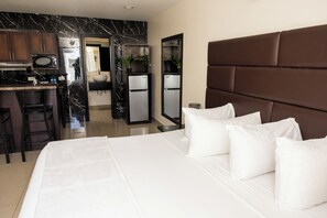 A hotel room with a bed, a headboard, a kitchen area with a refrigerator, and a bar. - Lovely Studio for Corporates (Charlotte Amalie West)