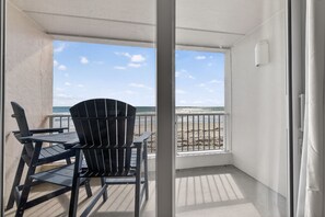 A balcony with a view of the beach, a table, and two chairs. - Sunrise Views & Sandy Toes – Beachfront Ponce Inlet Condo (Ponce Inlet)